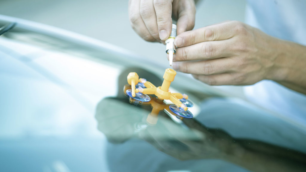 Eine Person repariert eine Autoscheibe mit einem orangefarbenen Werkzeug und einem Kleber, um einen Riss zu beheben.